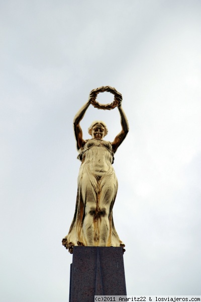 Detalle superior del Monumento Gëlle Fra (Dama Dorada)
Está en la Plaza de la Constitución.Consiste en un monumento de 21 metros de alto, un obelisco de granito que en la punta tiene una estatua de bronce con una mujer con corona de laureles cuya mirada se posa sobre toda la nación.

