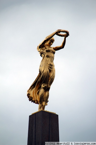 Lateral del Monumento Gëlle Fra (Dama Dorada)
Está en la Plaza de la Constitución.Consiste en un monumento de 21 metros de alto, un obelisco de granito que en la punta tiene una estatua de bronce con una mujer con corona de laureles cuya mirada se posa sobre toda la nación.
