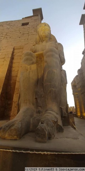 Estatua de Ramses II
La entrada al templo de Luxor es uno de los atractivos más impresionante del conjunto, en especial por la presencia de 2 grandiosas estatuas de Ramsés II de 14 metros de granito sentado, Ramses II se encuentra sentado con los brazos extendidos y las manos reposando sobre las rodillas. Entre sus pierna a un tamaño muy inferior puede contemplarse la imagen de su esposa Nefertari. Ante ellas se levanta un enorme obelisco y junto a él, se distingue el pedestal de otro. El obelisco que encontramos no es el verdadero, ya que el original se encuentra en Paris en la plaza de la concordia.
